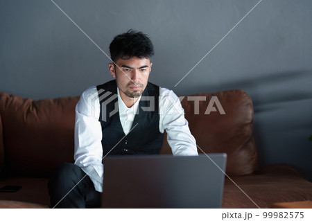 Portrait of a handsome, discreet Asian man sitting on the sofa using a computer. Portrait of a handsome, discreet Asian man sitting on the sofa using a computer. 99982575