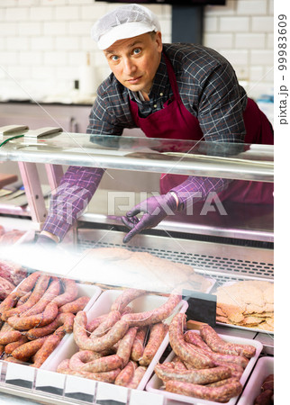 Butcher offering fresh raw sausages displayed in glass showcase 99983609