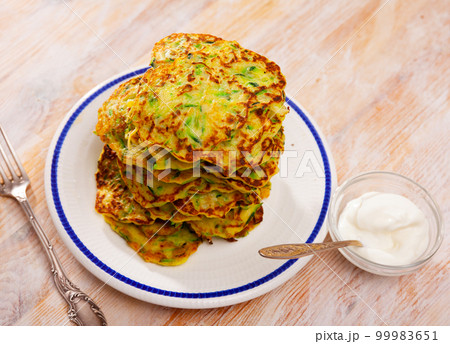 Zucchini pancakes served with sour cream 99983651