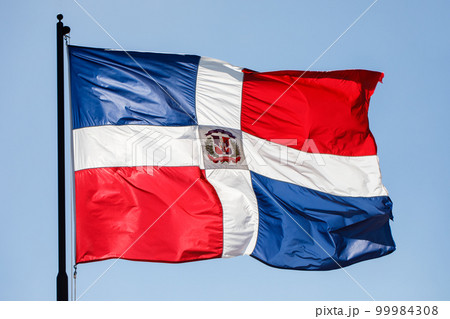 Dominican Republic flag waving against clear blue sky, close up, isolated. 99984308