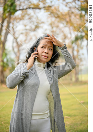 Confused 60s aged Asian woman on the phone, getting lost with her grandchild in the park. 99988161