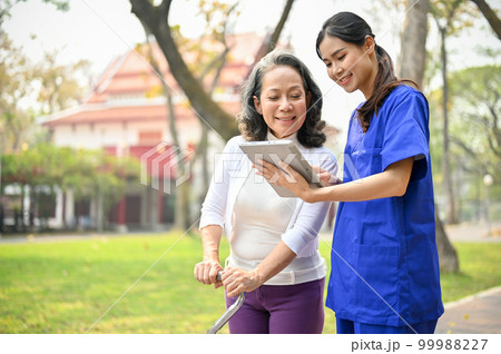 Asian female nurse or caregiver is showing something on her tablet screen to an old lady 99988227