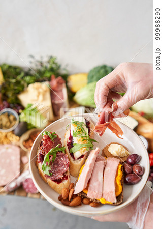 The waiter makes bruschetta or tapas. Table full of mediterranean appetizers, tapas or antipasto. Assorted Italian food set. Delicious snack on party or picnic time. Italian style banquet.  99988290