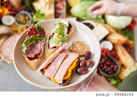 The waiter makes bruschetta or tapas. Table full of mediterranean appetizers, tapas or antipasto. Assorted Italian food set. Delicious snack on party or picnic time. Italian style banquet.  99988293