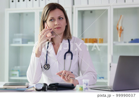 Female doctor calls her patient while sitting at table in medical clinic. 99990037
