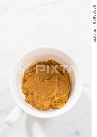 Pouring cake batter into the mug to prepare pumpkin mug cake. 99992629