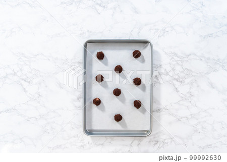 Flat lay. Scooping cookie dough with a small dough scoop into a baking sheet lined with parchment paper to bake peppermint white chocolate cookies. 99992630