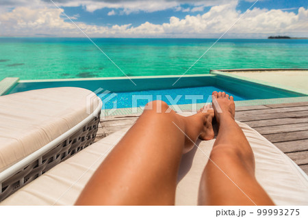 Suntan luxury vacation travel first person view woman sunbathing relaxing on sun lounger at hotel room. Feet selfie beach resort summer tropical travel destination swimming in blue water Suntan luxury vacation travel first person view woman sunbathing relaxing on sun lounger at hotel room. Feet selfie beach resort summer tropical travel destination swimming in blue water 99993275