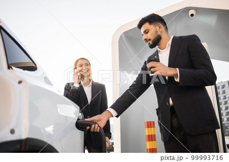 Diverse business partners charging electric car on station 99993716