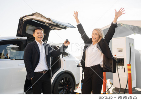 Cheerful woman receiving keys from her new electric car Cheerful woman receiving keys from her new electric car 99993925