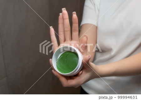 Young girl shows eye patches. Caring for the skin under the eyes. Gray background. 99994631