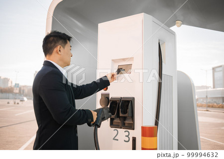 Asian man using credit card at EV charging station 99994632