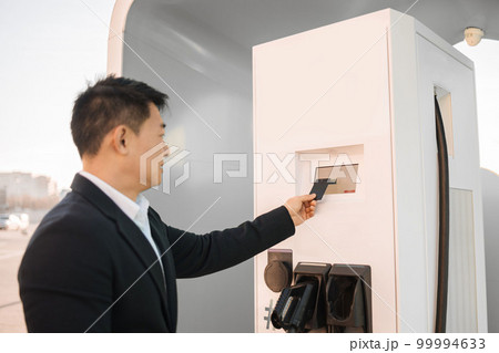 Asian man using credit card at EV charging station 99994633