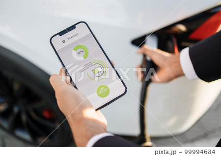 Close up of man charging electric car and using smartphone Close up of man charging electric car and using smartphone 99994684
