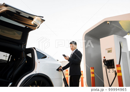 Happy man charging electro car and using smartphone Happy man charging electro car and using smartphone 99994965
