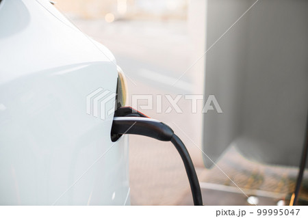 Electric car with plug cord connected to charging port Electric car with plug cord connected to charging port 99995047
