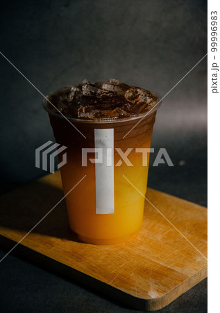 Close up of americano and orange juice in plastic glass with white sticker tag on wooden plate with gray background 99996983