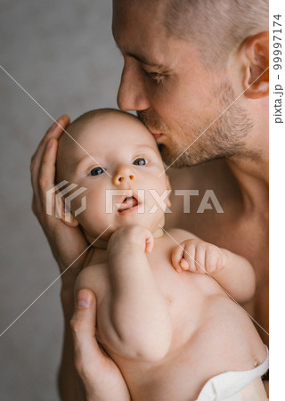 A young father holds his newborn son in a diaper in his arms and kisses him 99997174