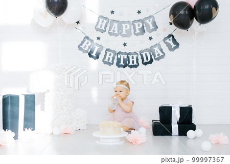 Birthday girl 1 year sitting in the photo zone surrounded by gifts, flowers 99997367