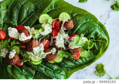 Falafel wrap with vegetables and tahini on chard lettuce. Alternative vegan recipe. Falafel wrap with vegetables and tahini on chard lettuce. Alternative vegan recipe. 99998165