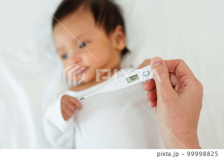 mother measuring temperature of her ill baby. sick child with high fever on bed mother measuring temperature of her ill baby. sick child with high fever on bed 99998825