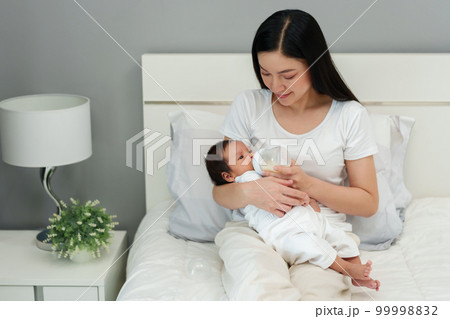 mother feeding milk bottle to her newborn baby on bed mother feeding milk bottle to her newborn baby on bed 99998832