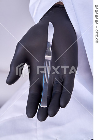 Hand in a surgical glove holding a scalpel. Vertical shot close up. 99999090