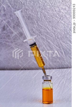 Syringe with golden glitters sticks in a vaccine bottle. Vertical shot close up. 99999243