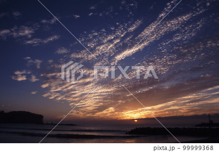 太陽が顔をだし、雲をオレンジ色に染め、ドラマチックな海岸の夜明けが綺麗だ。 99999368