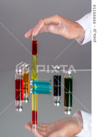 Hand with glove holding test tube with blood. Drug vials with colored solution. Colorful vaccine bottles. Hand with glove holding test tube with blood. Drug vials with colored solution. Colorful vaccine bottles. 99999559