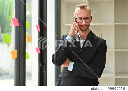 Portrait of millennial male business executive having phone conversation while standing in modern office 99999956
