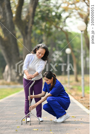 Attentive practitioner nurse assisting senior female walking with tripod cane. Assistance, rehabilitation and health 100000051
