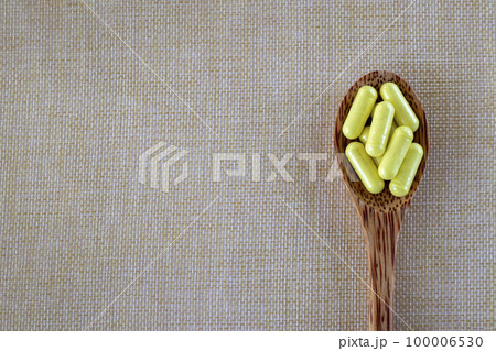 Capsules yellow Quercetin in a wooden spoon on a beige background. Top view, copy space. 100006530