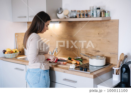 Back view of young beautiful woman is preparing lunch in her kitchen at home Back view of young beautiful woman is preparing lunch in her kitchen at home 100011100
