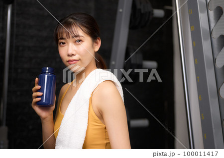 ドリンクを持ちながら視線を向けるスポーツウェア姿の若い女性 100011417