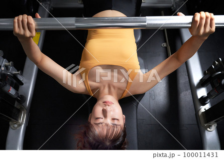 ジムにてベンチプレスで筋力トレーニングをする若い女性 100011431