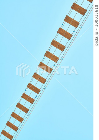 Long rope bridge with wooden planks against clear blue sky. Fun attraction for tourists in recreational water park at summer resort Long rope bridge with wooden planks against clear blue sky. Fun attraction for tourists in recreational water park at summer resort 100013618
