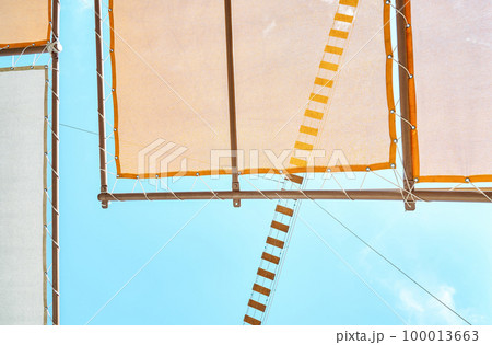 Canopy and rope bridge in recreational area of water park against clear blue sky. Orange sun-protection cover above deck chairs closeup 100013663