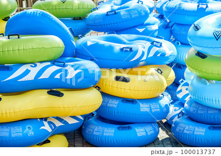 Multi-colored rubber rings for swimming pool put in rows at bright sunlight. Stacks of inflatable swim-rings ready for tourists in water park Multi-colored rubber rings for swimming pool put in rows at bright sunlight. Stacks of inflatable swim-rings ready for tourists in water park 100013737