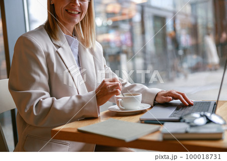 Close up of woman freelancer working on laptop and drinking coffee while sitting in cafe near window Close up of woman freelancer working on laptop and drinking coffee while sitting in cafe near window 100018731