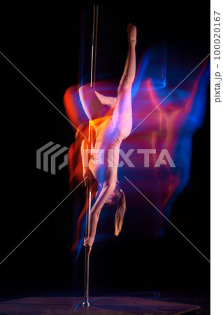 Artistic lifestyle. Young girl in bodysuit performing pole dance isolated over black studio background with mixed neon lights. Concept of art, sport and modern dance 100020167