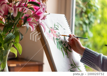 Young girl painting still life with flowers, purple lilies, with watercolor paints on the easel Young girl painting still life with flowers, purple lilies, with watercolor paints on the easel 100020732