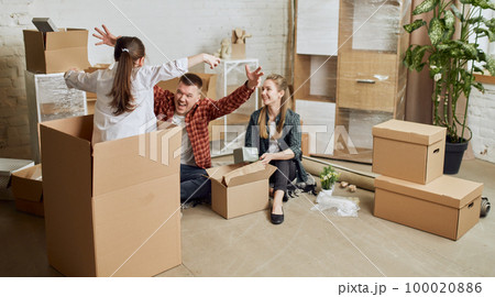 Young happy family, man, woman and kid moving into new flat, apartment with many cardboard boxes. Father playing with little daughter 100020886
