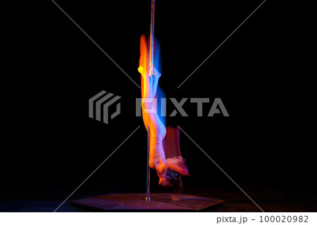 Upside down. Line. Young girl performing pole dance isolated over black studio background with mixed neon lights. Concept of art, sport and modern dance Upside down. Line. Young girl performing pole dance isolated over black studio background with mixed neon lights. Concept of art, sport and modern dance 100020982