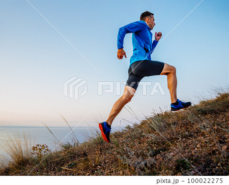 male runner running uphill in background sky and sea 100022275