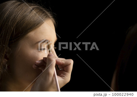 Makeup artist doing a eyebrows makeup on a beautiful woman face. Hand of make-up master is painting eyebrow of young beauty model girl. Make up in process. Makeup artist doing a eyebrows makeup on a beautiful woman face. Hand of make-up master is painting eyebrow of young beauty model girl. Make up in process. 100022940