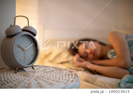 The girl in bed sleeps in the bedroom with an alarm clock on the cabinet next to her. 100023615