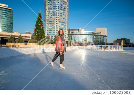 a young beautiful girl on skates in a sheepskin coat on a skating rink against the backdrop of the metropolis and the rays of the sun a young beautiful girl on skates in a sheepskin coat on a skating rink against the backdrop of the metropolis and the rays of the sun 100025008