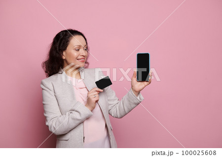 Pretty woman in formal suit, confident successful business lady, entrepreneur, sales manager or bank client, smiling and showing at camera a black credit card and smartphone, on isolated background Pretty woman in formal suit, confident successful business lady, entrepreneur, sales manager or bank client, smiling and showing at camera a black credit card and smartphone, on isolated background 100025608
