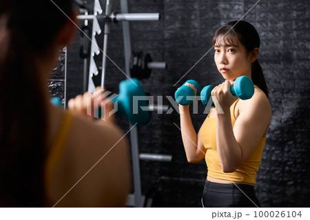 ダンベルを使ってトレーニングをする若い女性 ダンベルを使ってトレーニングをする若い女性 100026104